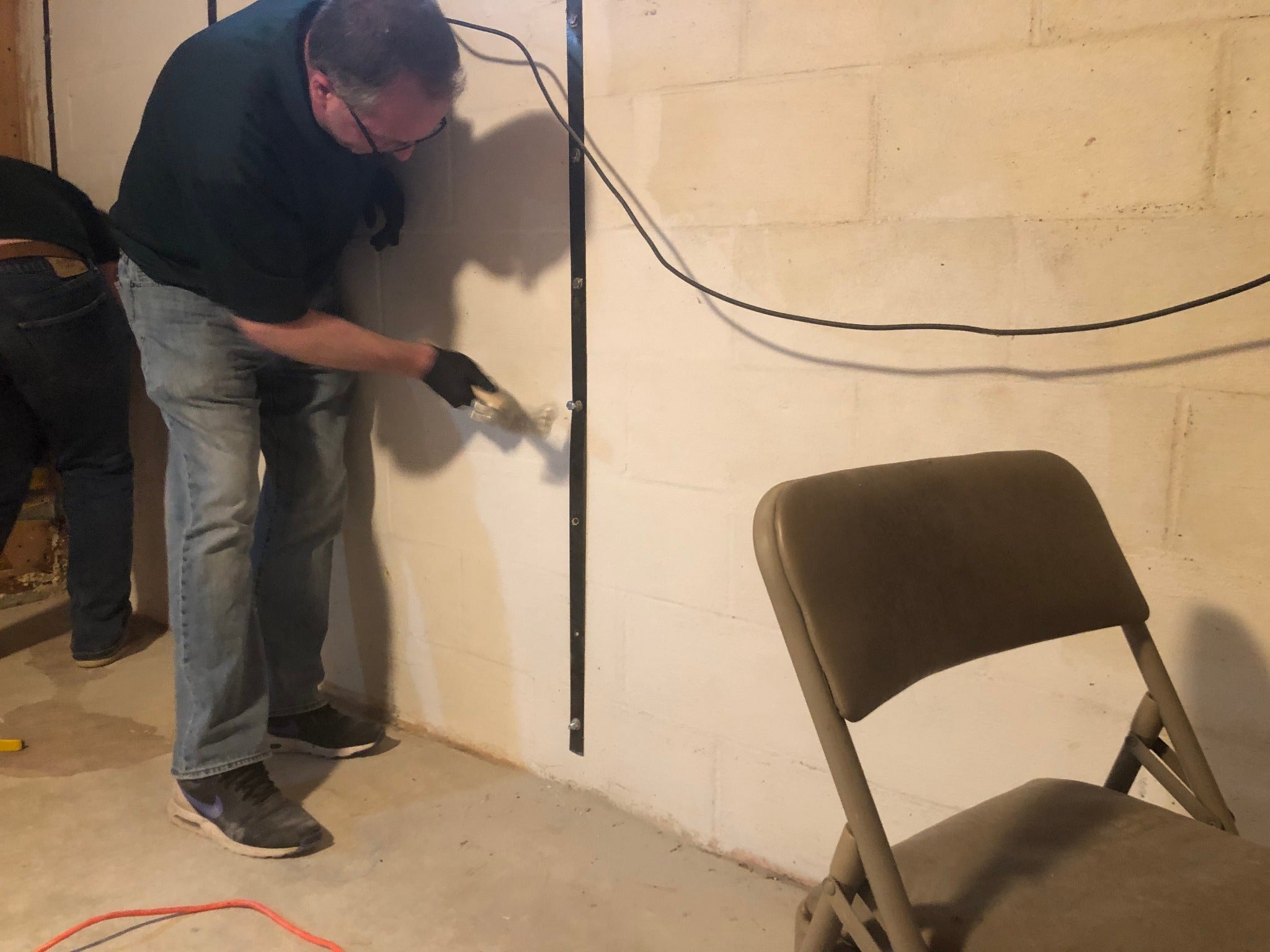 Installer fastening a Nolan Basement Wall Strap to a concrete block foundation wall